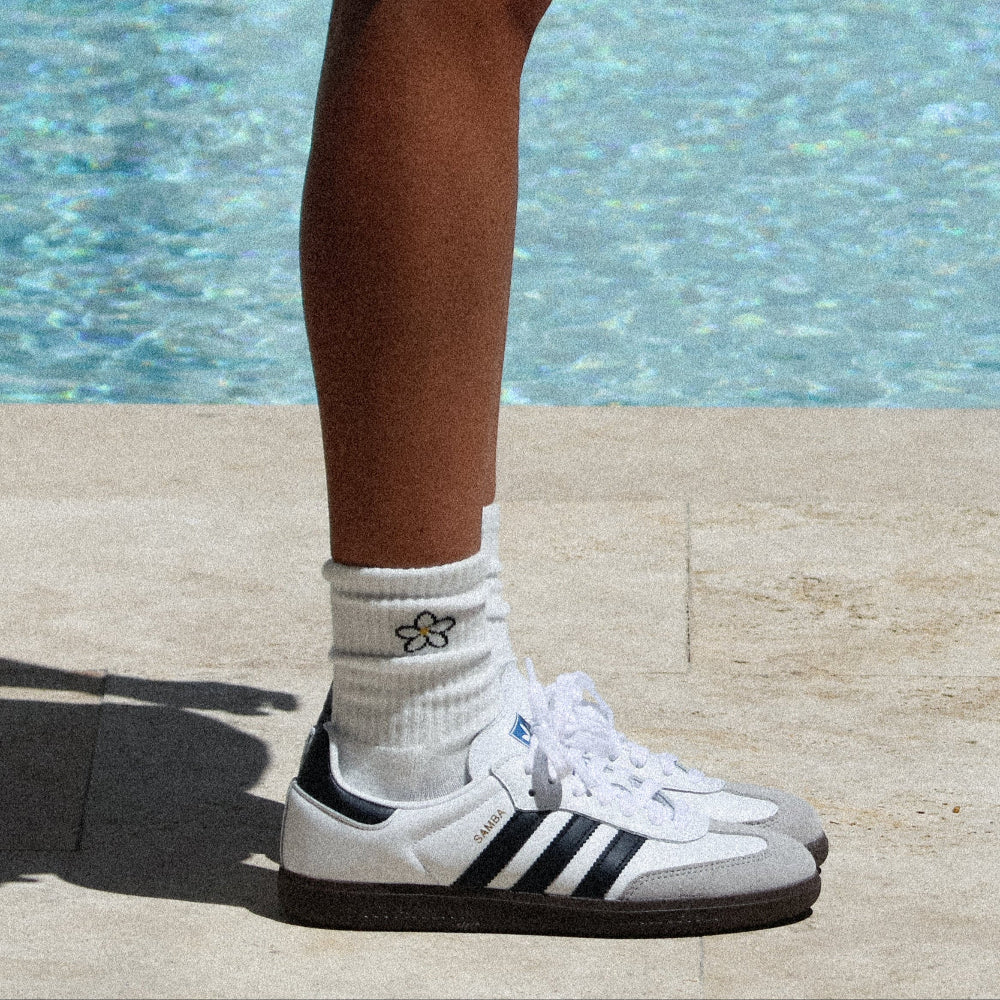 Person wearing white sneakers with black stripes by a pool